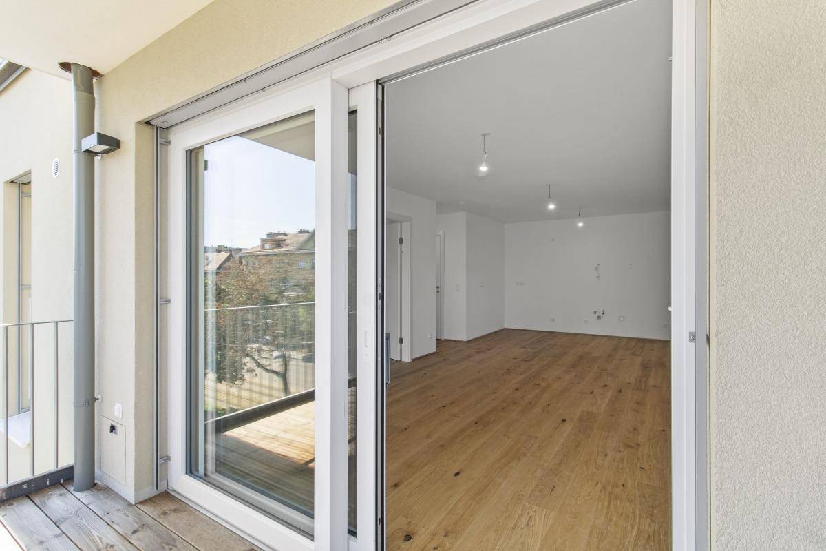 Blick aus dem Innenraum durch eine große Schiebetür auf den Balkon mit Stadtansicht.