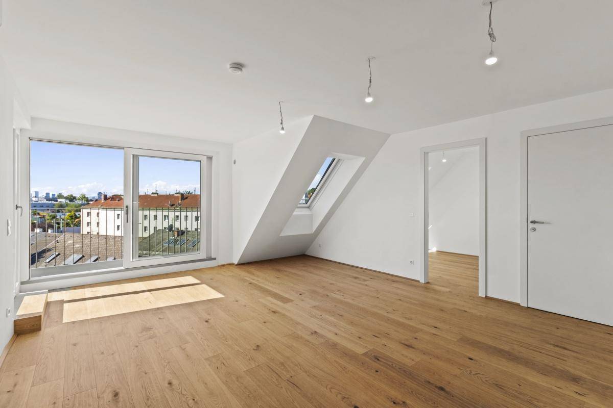 Heller Wohnbereich mit Holzboden, großen Fenstern, Dachschräge und Zugang zum Balkon.