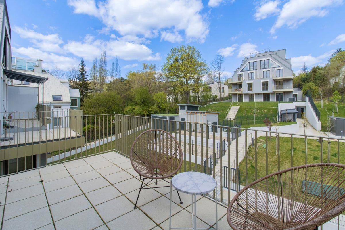 Balkon mit Sitzgelegenheiten und Blick auf die grüne Umgebung und weitere Gebäude.