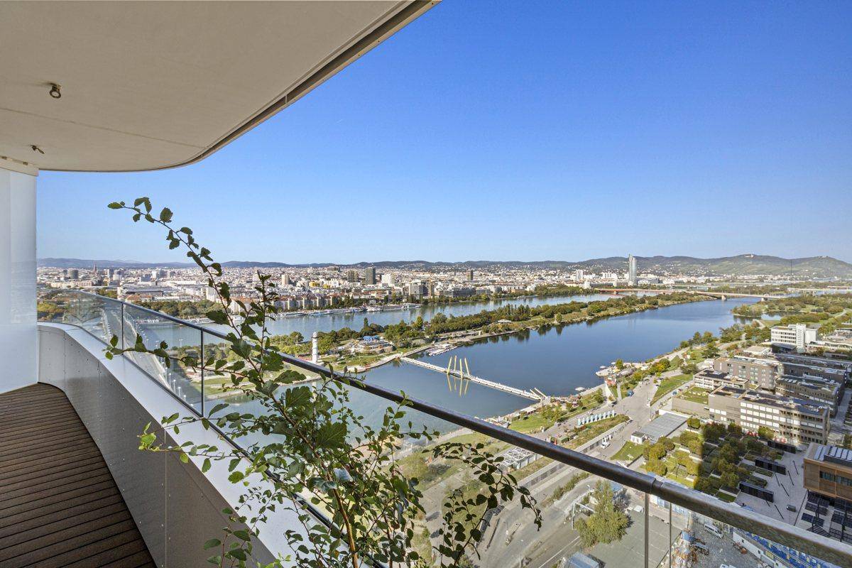 Großer Balkon mit Holzdeck und Glasgeländer, bietet einen atemberaubenden Stadt- und Flussblick.