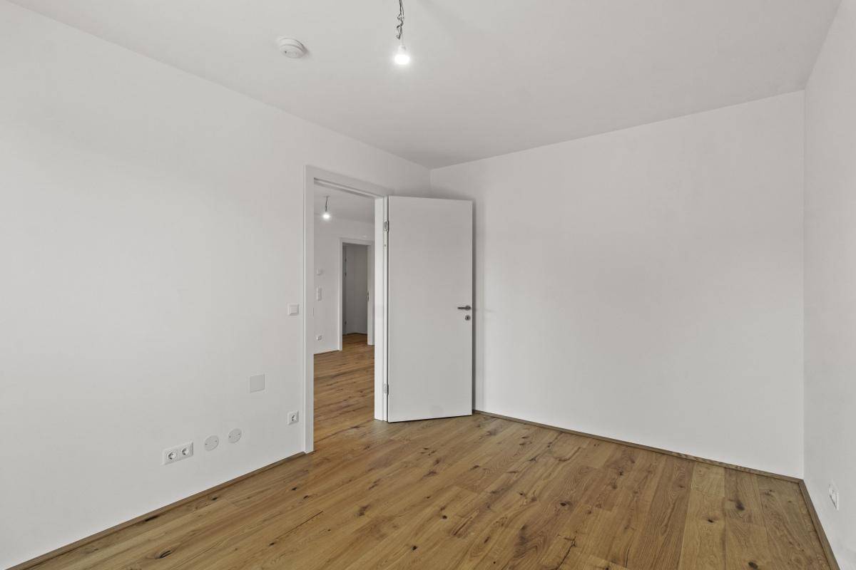 Helles, leeres Zimmer mit Holzboden und weiß gestrichenen Wänden, bereit zur Einrichtung.
