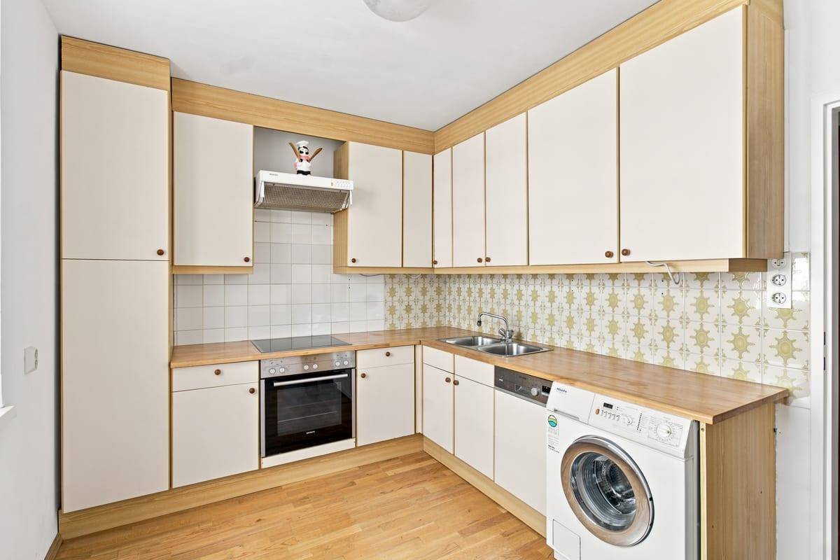 Funktionale Küche mit hellen Holzfronten, integriertem Backofen und Waschmaschine.