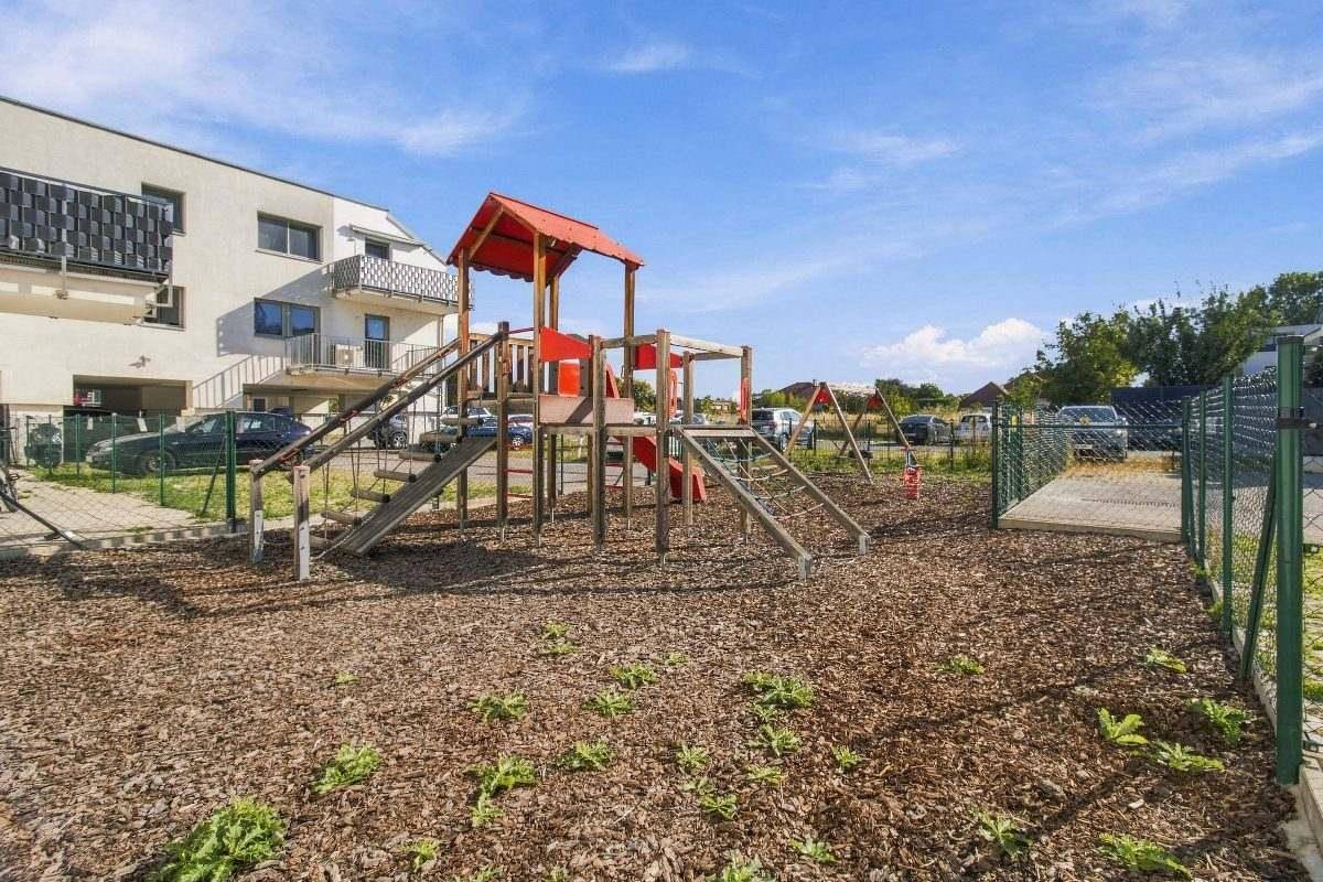 Kinderspielplatz mit Rutsche und Schaukeln, umgeben von einer sicheren Holzmulchfläche.