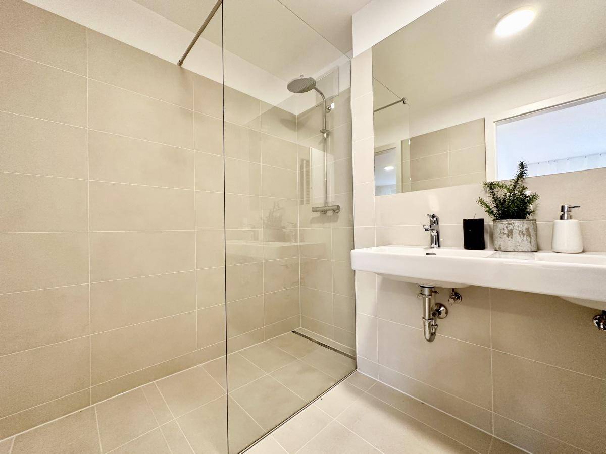 Helles Badezimmer mit begehbarer Dusche, modernem Waschbecken und großem Spiegel.