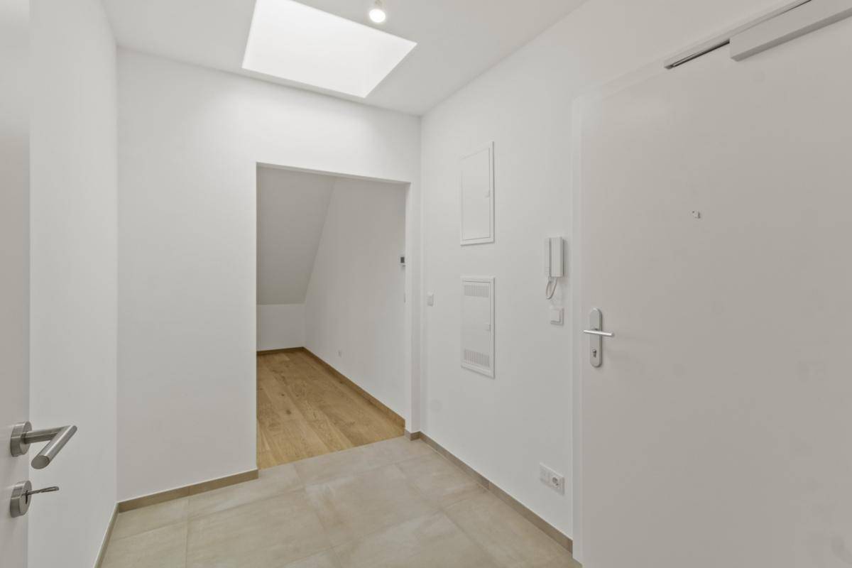 Heller Eingangsbereich mit Fliesenboden, weißen Wänden und einem Oberlicht für Tageslicht.
