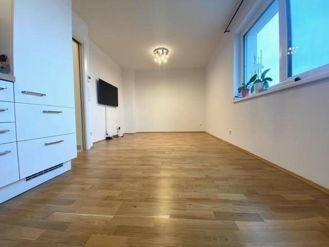 Heller Wohnbereich mit Holzparkettboden und großem Fenster, bereit zur individuellen Gestaltung.