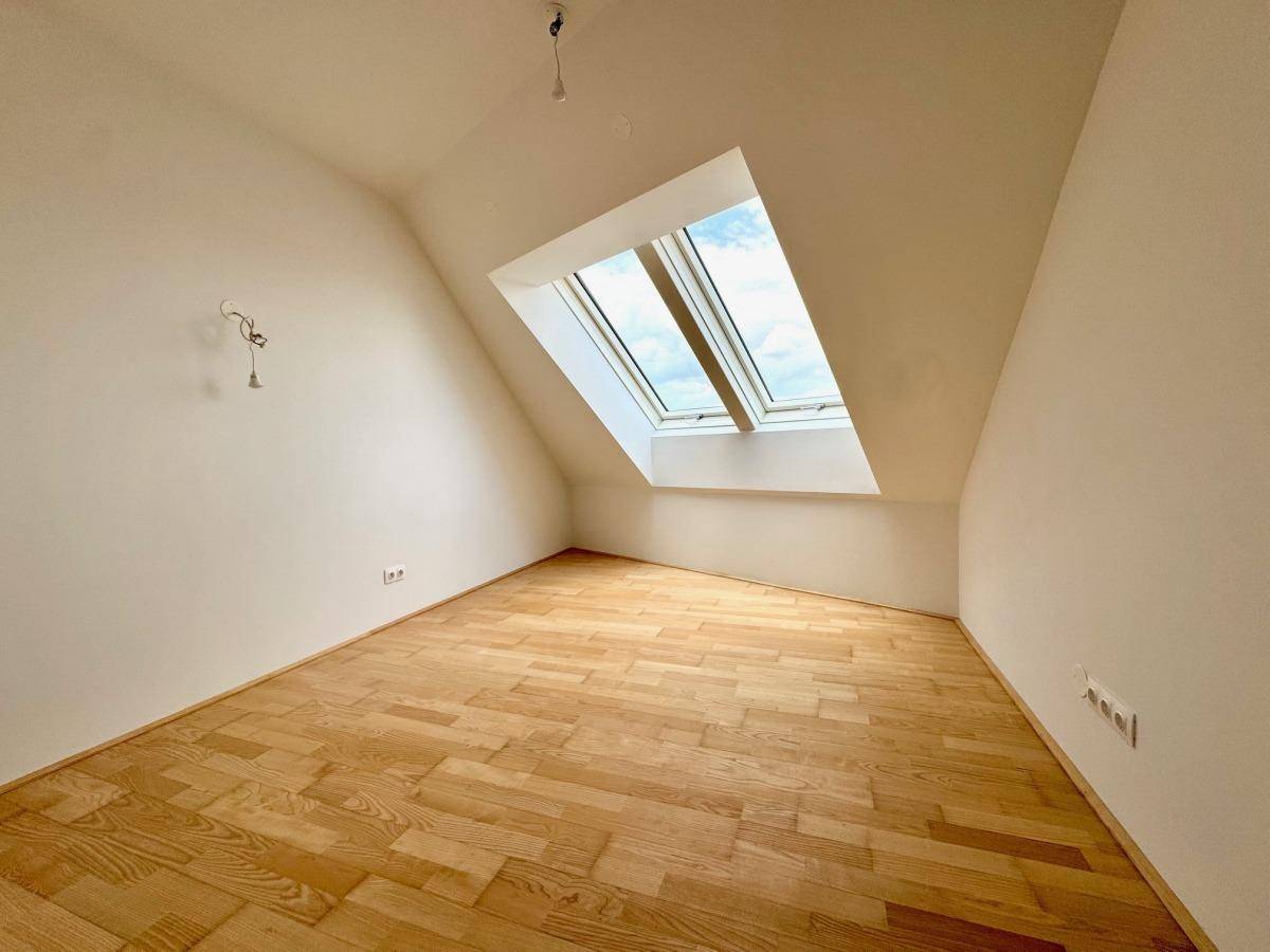 Helles Zimmer mit Holzparkettboden und einem großen Dachfenster, das viel Tageslicht hereinlässt.