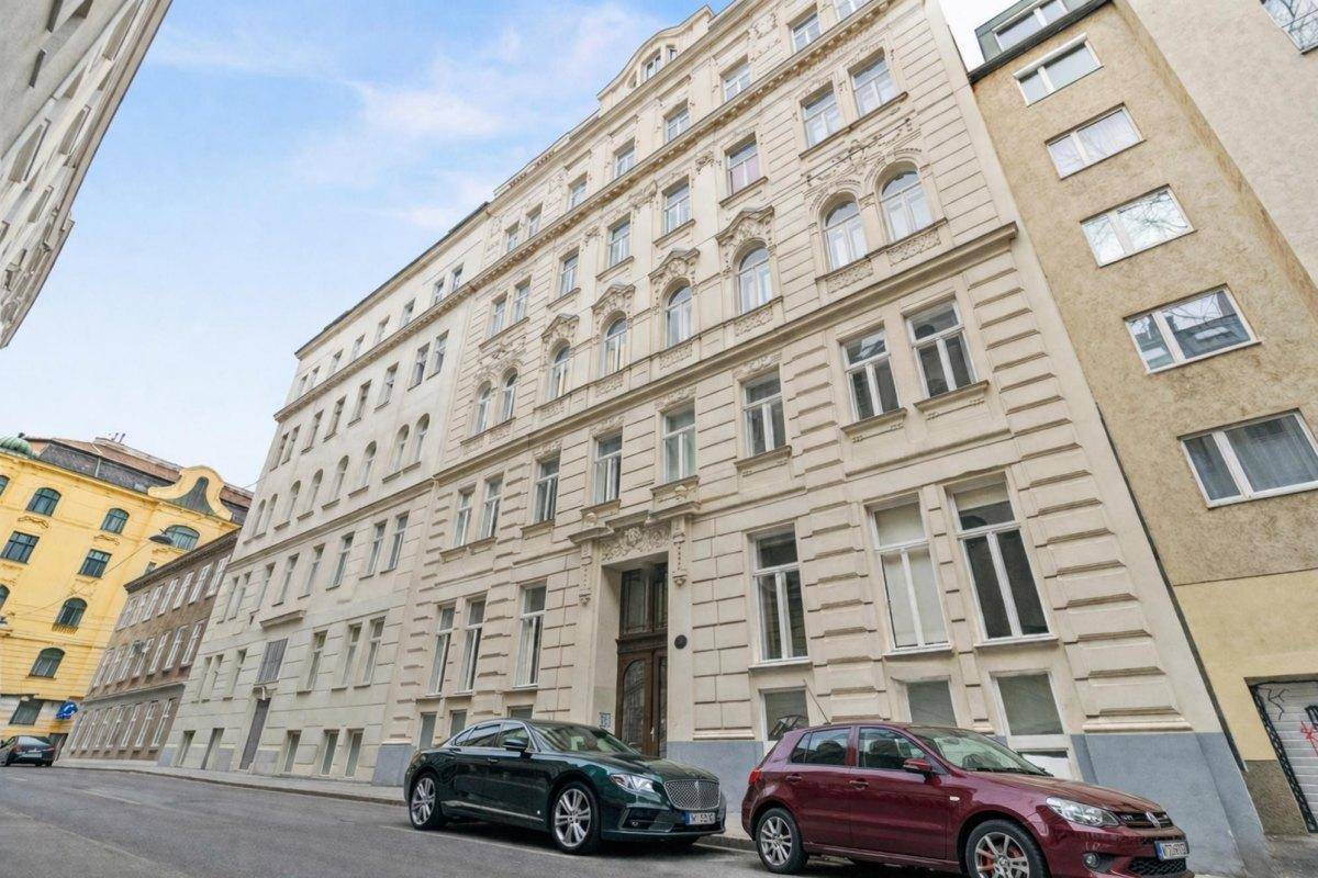 Weitwinkelansicht eines historischen Gebäudes an einer Straße mit parkenden Autos und klarem Himmel.