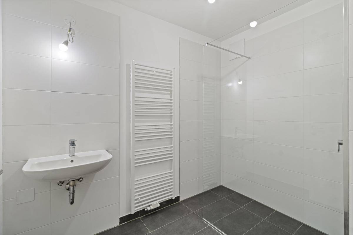 Modernes Badezimmer mit weiß gefliesten Wänden, Dusche, Waschbecken und Handtuchheizkörper.