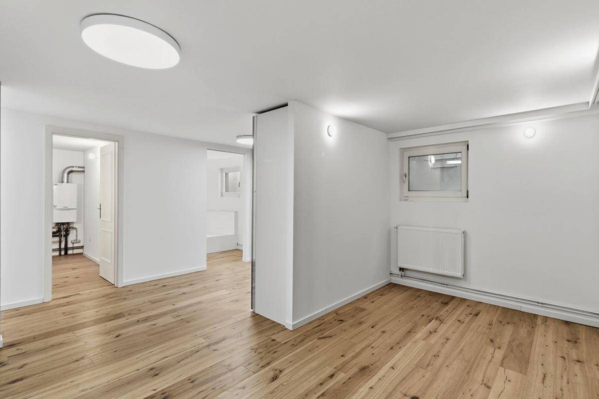 Ausgebauter Kellerraum mit Holzboden, Fenster und Zugang zu einem Technikraum.