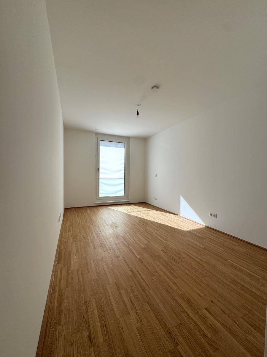 Helles Schlafzimmer mit Parkettboden und einem großen Fenster, bereit zur Einrichtung.