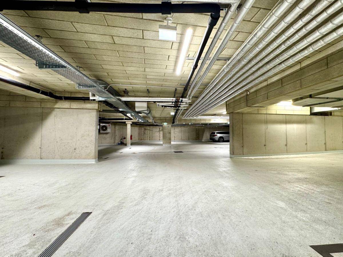 Geräumige Tiefgarage mit Betonboden, sichtbaren Leitungen und ausreichend Platz für Fahrzeuge.