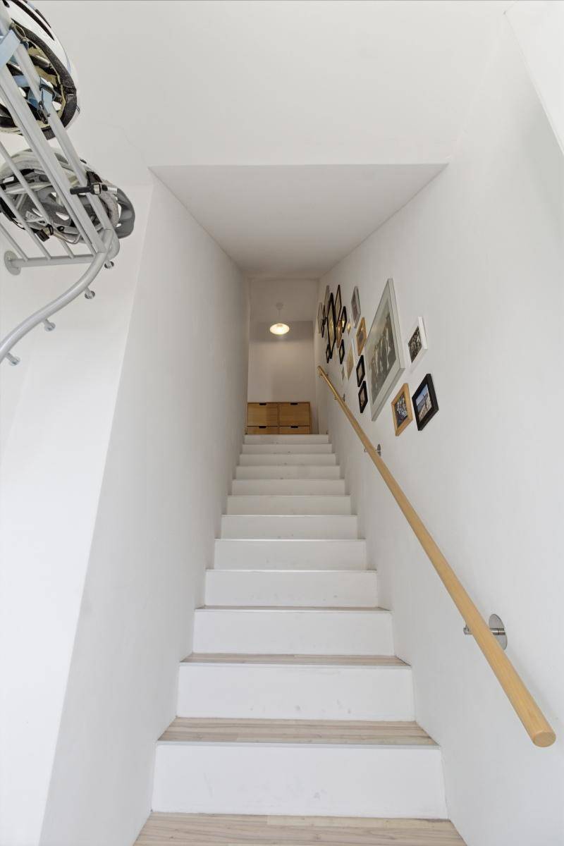 Treppenaufgang mit weiß gestrichenen Wänden, Holzgeländer und dekorativen Bildern an der Wand.