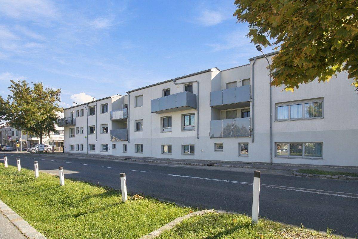 Ansicht eines modernen Mehrfamilienhauses von der Straße mit Balkonen und weißer Fassade.