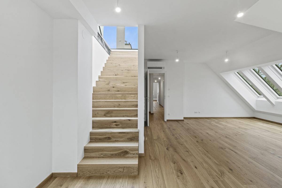 Geräumiges Dachgeschoss mit Holztreppe, hellem Holzboden und Zugang zu weiteren Räumen.