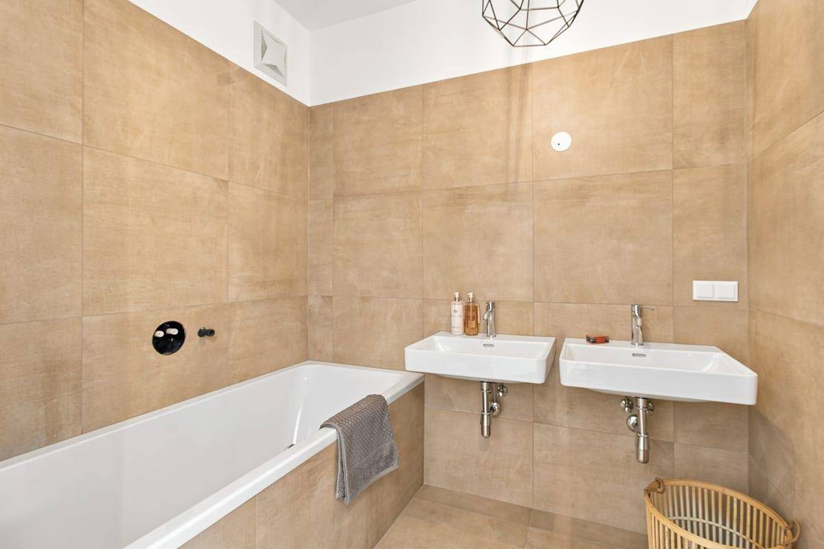 Modernes Badezimmer mit beigefarbenen Fliesen, Badewanne und Doppelwaschbecken.