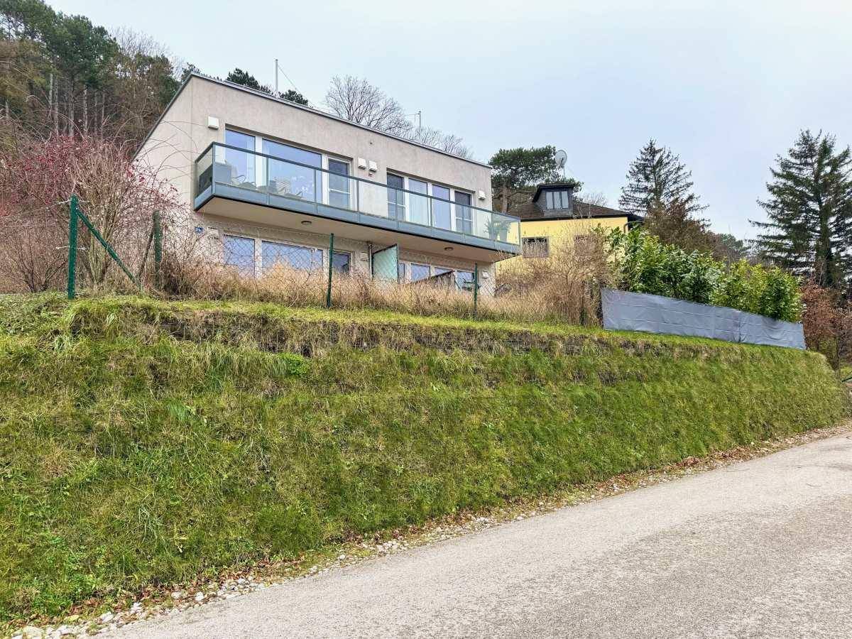 Modernes Wohnhaus mit Balkonen und großen Fenstern, gelegen an einem Hang mit Blick auf die Umgebung.