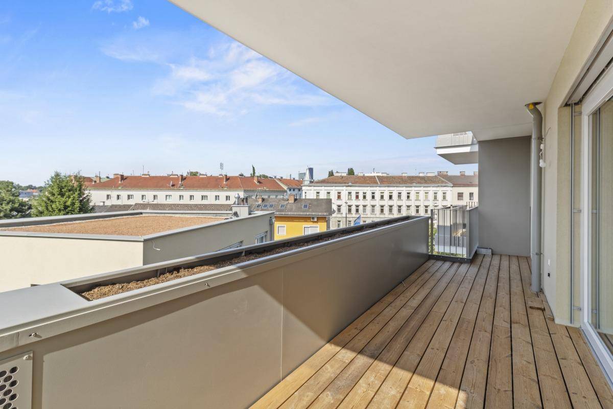 Geräumiger Balkon mit Holzdielen, Pflanzkübel und weitem Blick über die Stadt.