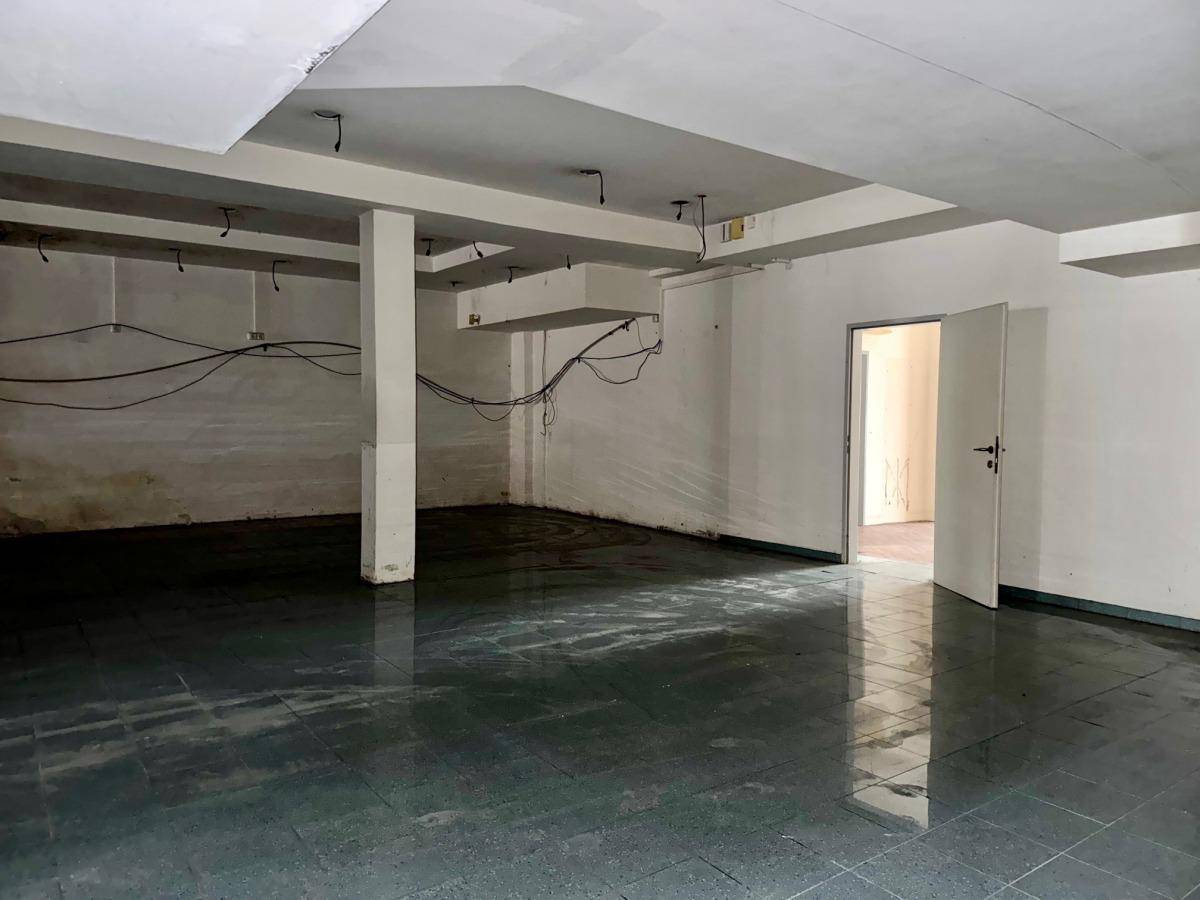 Großer leerer Raum mit Fliesenboden, Säulen und sichtbaren Kabeln an der Wand.