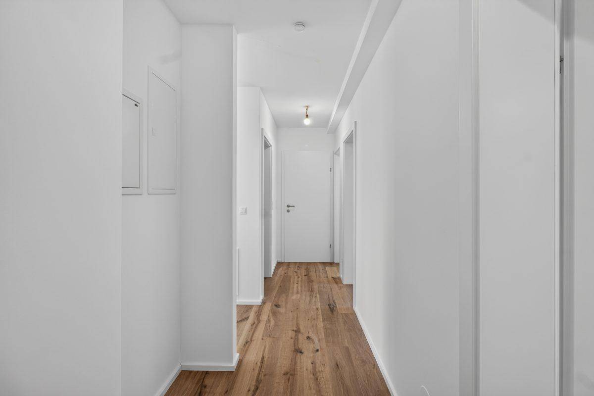 Heller Flur mit modernem Holzparkettboden und weißen Wänden.