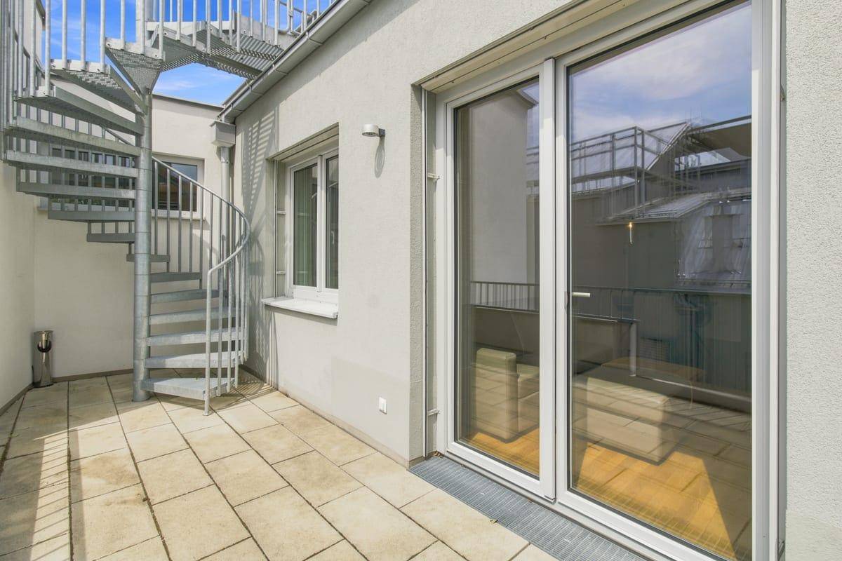 Heller Balkon mit Steinplatten und einer Wendeltreppe, die zur Dachterrasse führt.