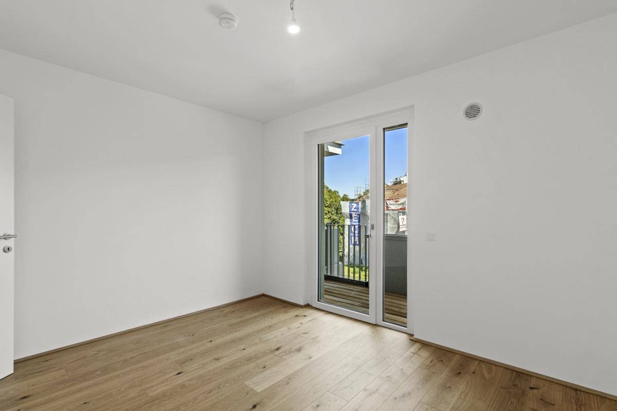 Helles Zimmer mit Holzboden und Zugang zum Balkon, ideal als Schlaf- oder Arbeitszimmer.