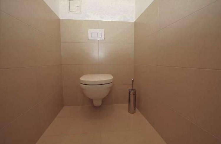 Separates WC mit wandhängender Toilette und beigefarbenen Fliesen an Wänden und Boden.