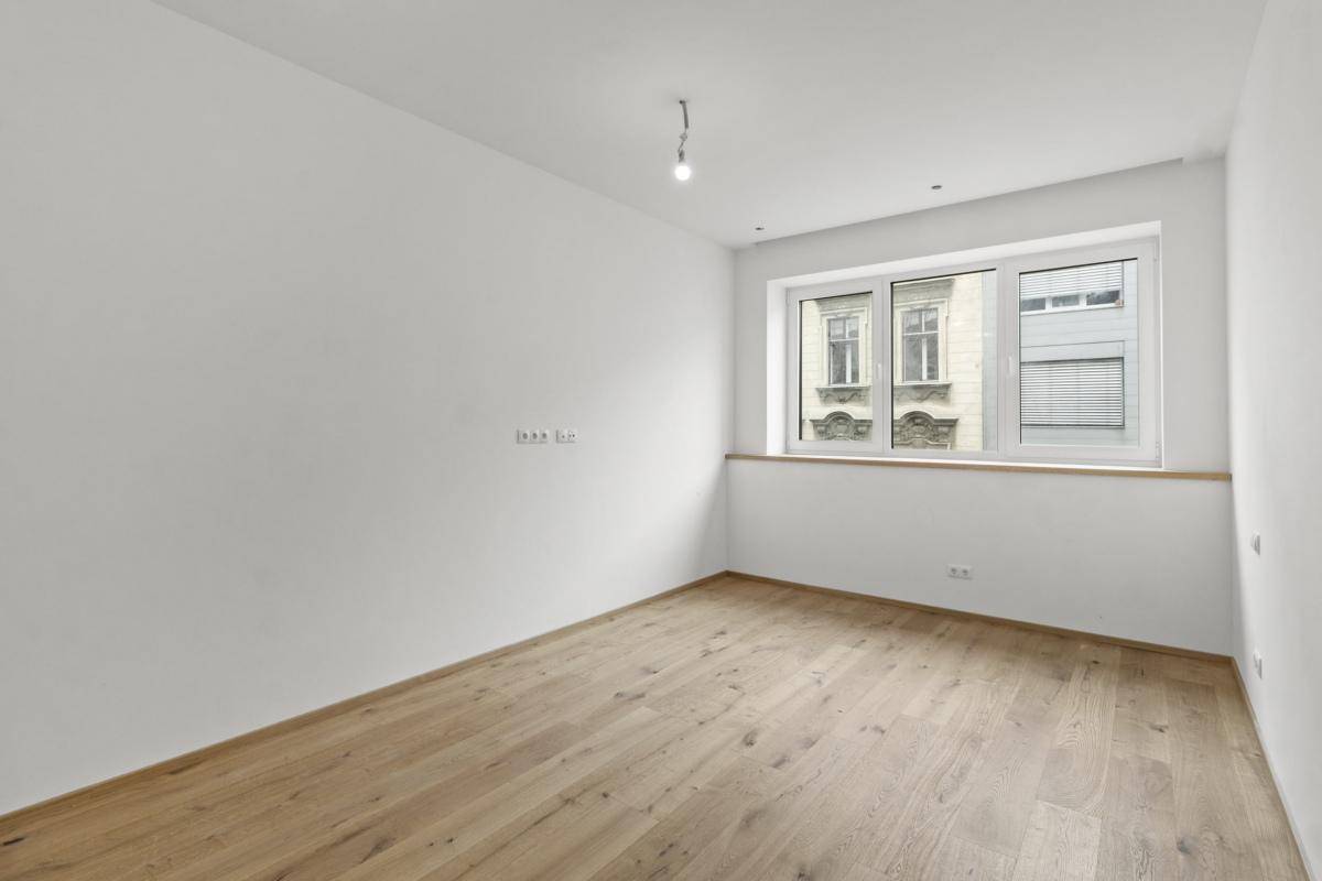 Helles Schlafzimmer mit Holzboden und einem Fenster, das den Blick auf die umliegenden Gebäude freigibt.