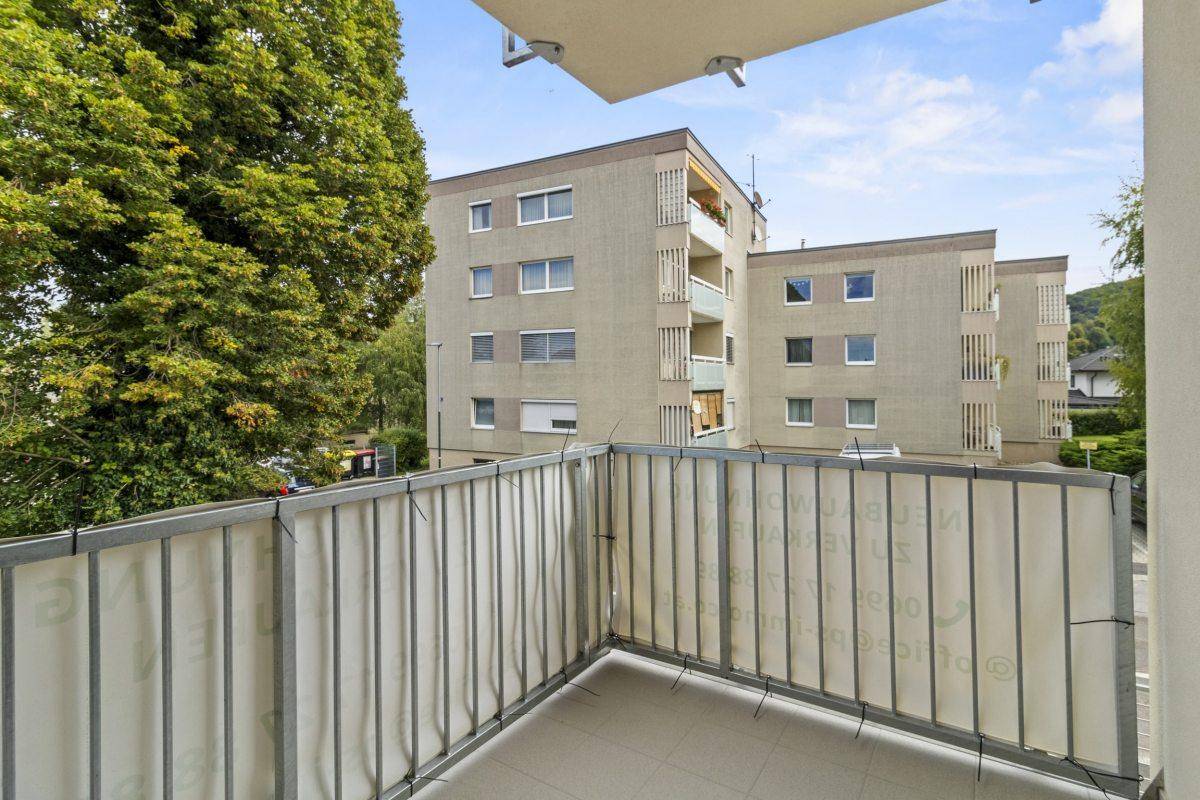 Balkon mit Fliesenboden und Blick auf ein gegenüberliegendes Gebäude und Bäume.