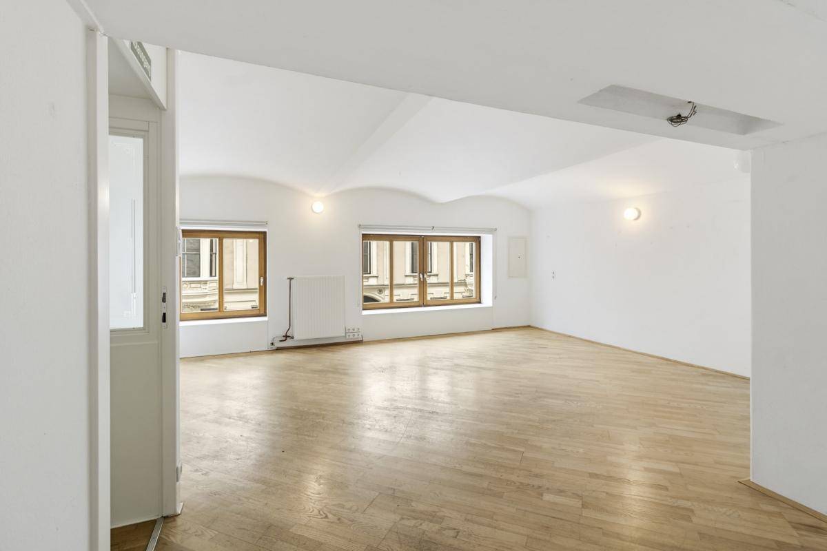 Heller Büroraum mit Holzboden, hohen Decken und großen Fenstern mit Blick auf die Stadt, viel Tageslicht.