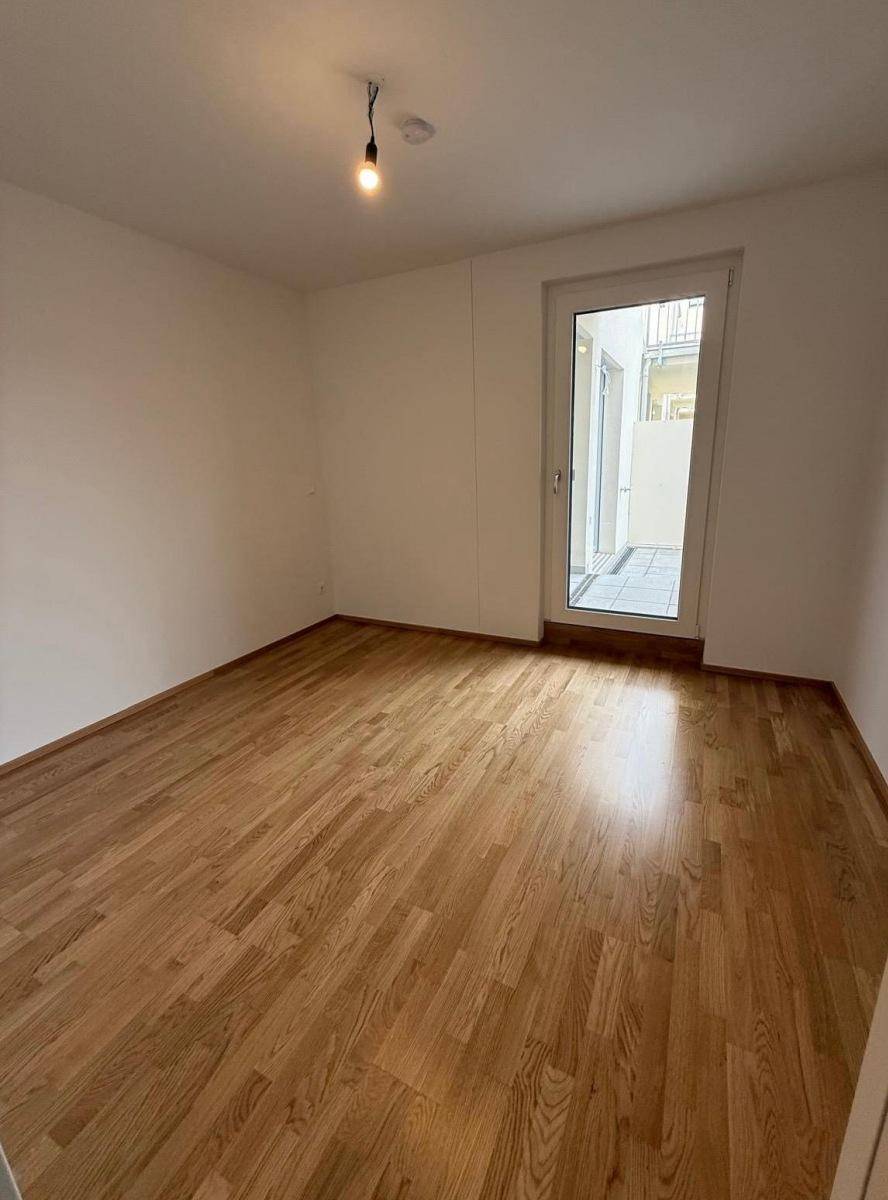 Schlafzimmer mit hellem Parkettboden und Zugang zu einem Außenbereich.