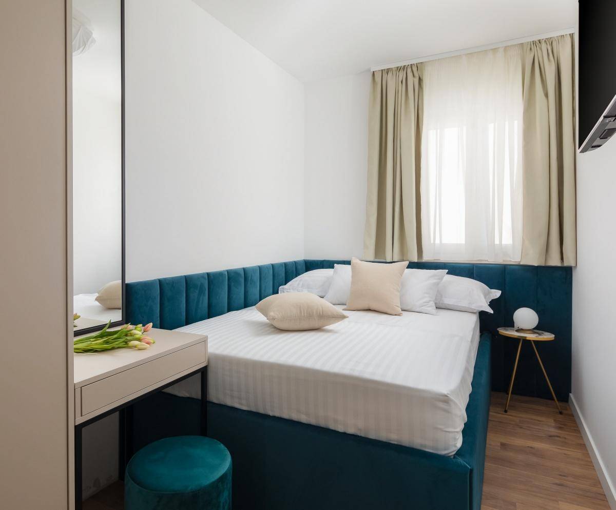 Helles Schlafzimmer mit blauem Bett, Schminktisch und Holzboden, gut beleuchtet.