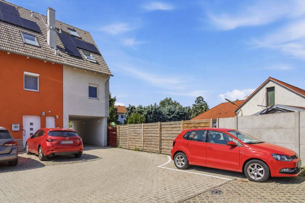 Parkplätze vor einem modernen Reihenhaus mit Photovoltaikanlage und angrenzendem Zaun.