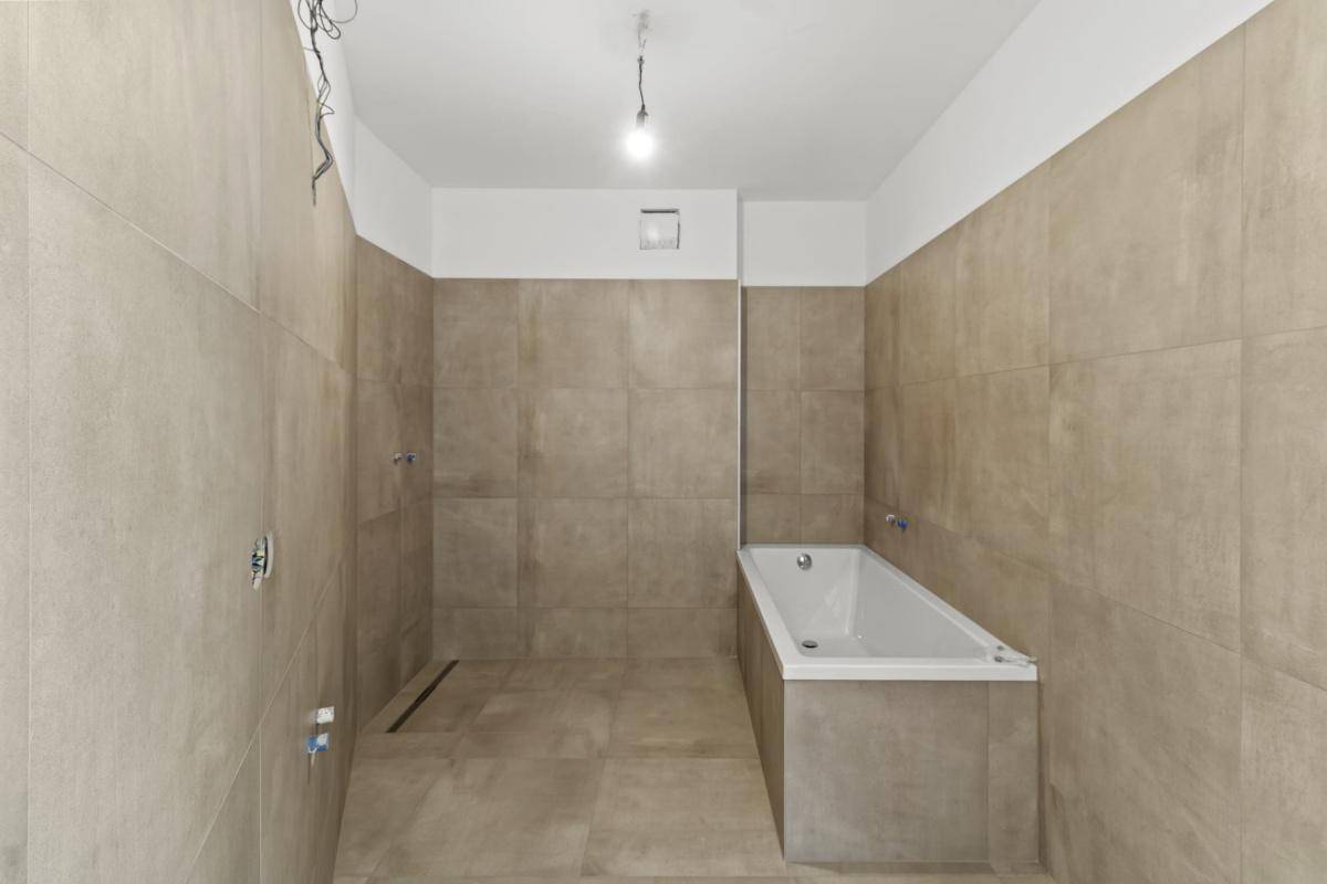 Modernes Badezimmer mit beigefarbenen Fliesen, Badewanne und vorbereiteten Anschlüssen.