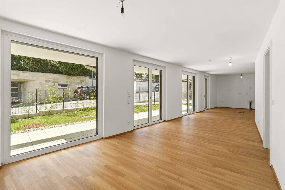 Heller, leerer Raum mit großen Fenstern und hochwertigem Holzparkettboden.