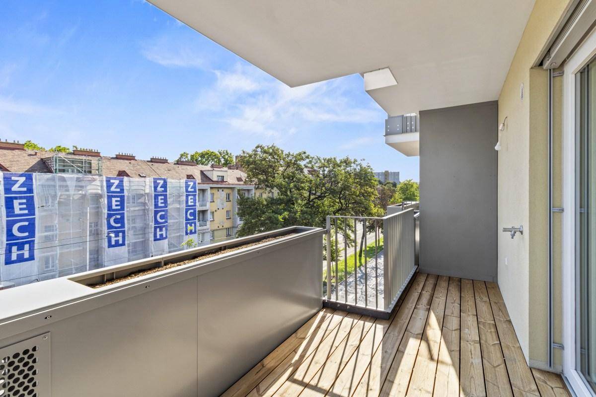 Geräumiger Balkon mit Holzboden und Blick auf die umliegenden Gebäude und Grünflächen.