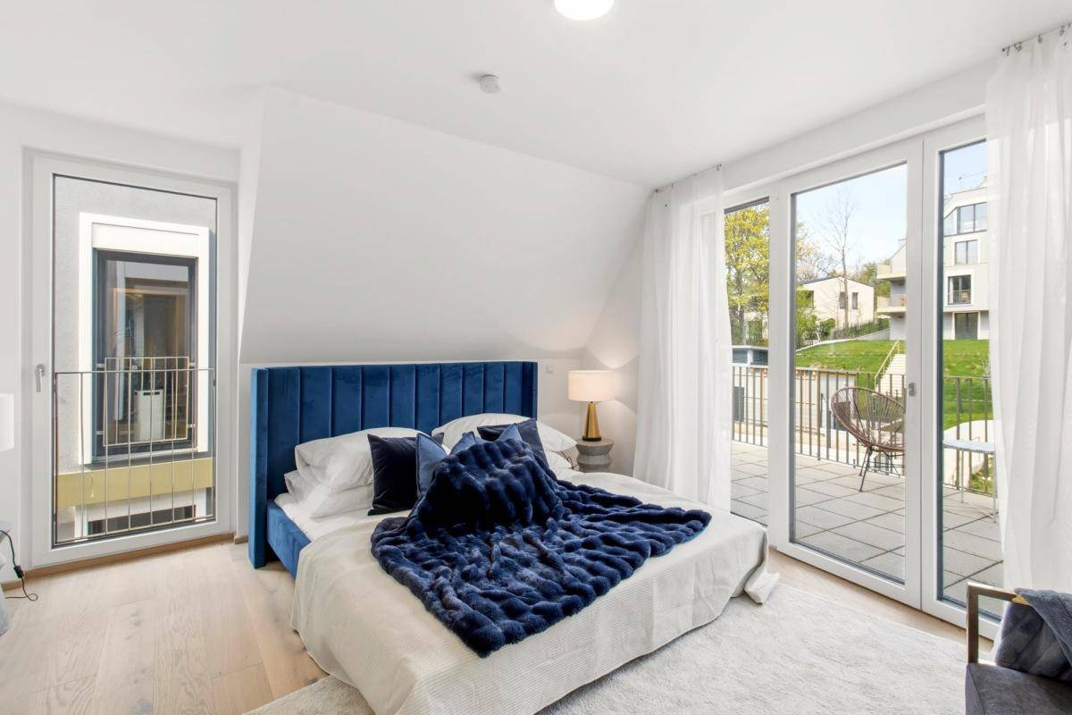 Helles Schlafzimmer mit blauem Bett, Holzboden und Zugang zu Balkon und Terrasse.