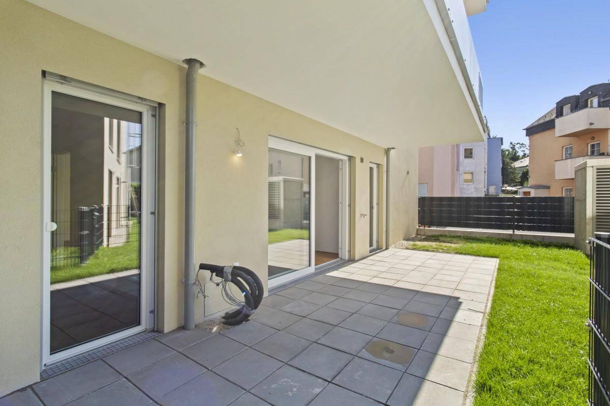 Helle, unmöblierte Terrasse mit Fliesenboden und angrenzender Rasenfläche.