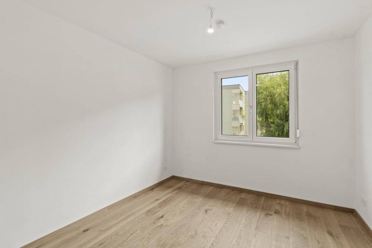 Helles Schlafzimmer mit Parkettboden und einem Fenster mit Blick ins Grüne.
