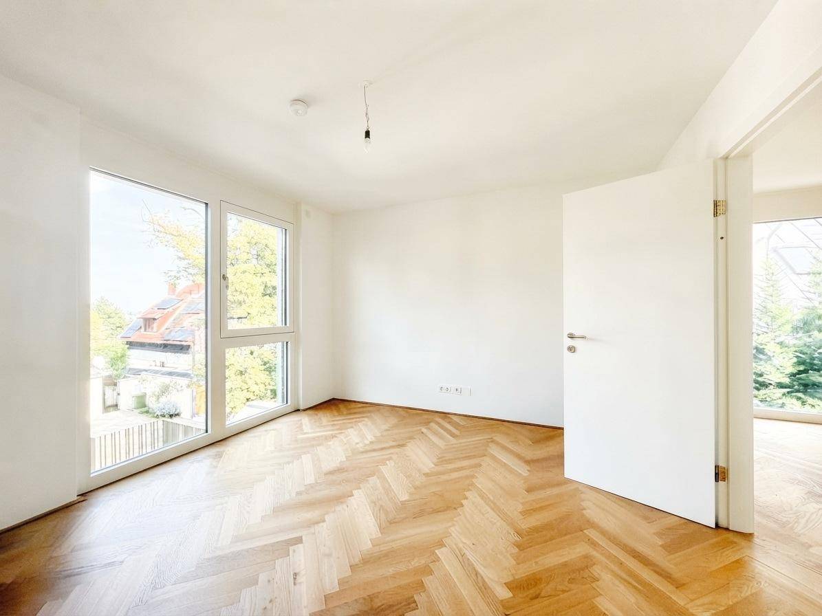 Geräumiges Schlafzimmer mit Fischgrätparkett und großen Fenstern, die einen Blick ins Grüne bieten.