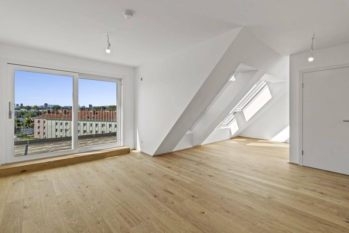 Geräumiger Dachgeschossraum mit Holzboden, Zugang zu einem Balkon und mehreren Dachfenstern.