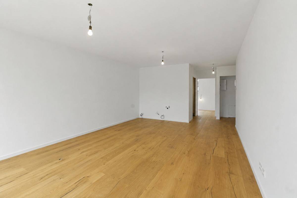 Heller Raum mit Holzboden und weiß gestrichenen Wänden, offen zum Flurbereich.