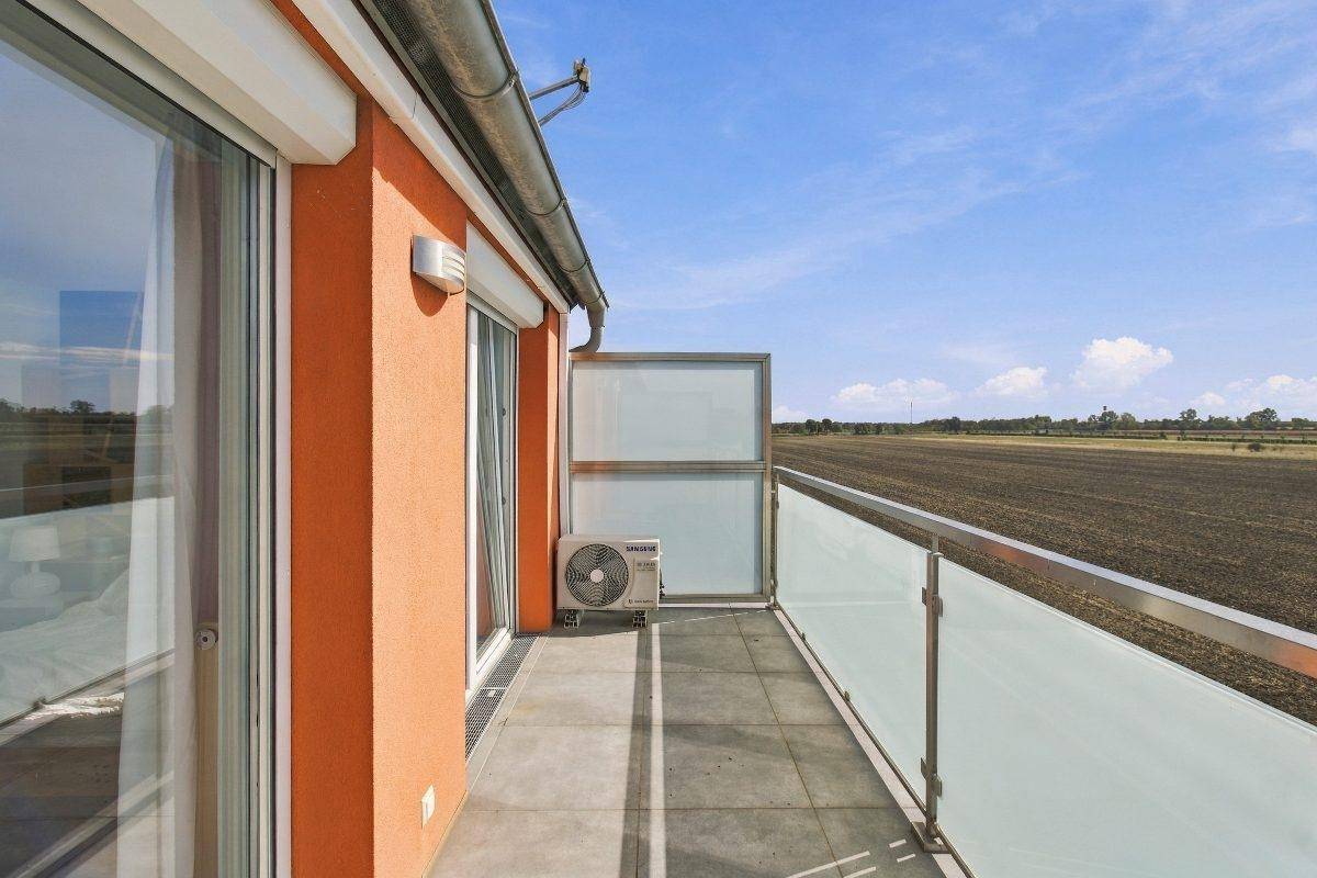 Balkon mit Glasbrüstung, Klimaanlage und weitem Blick über Felder und Landschaft.