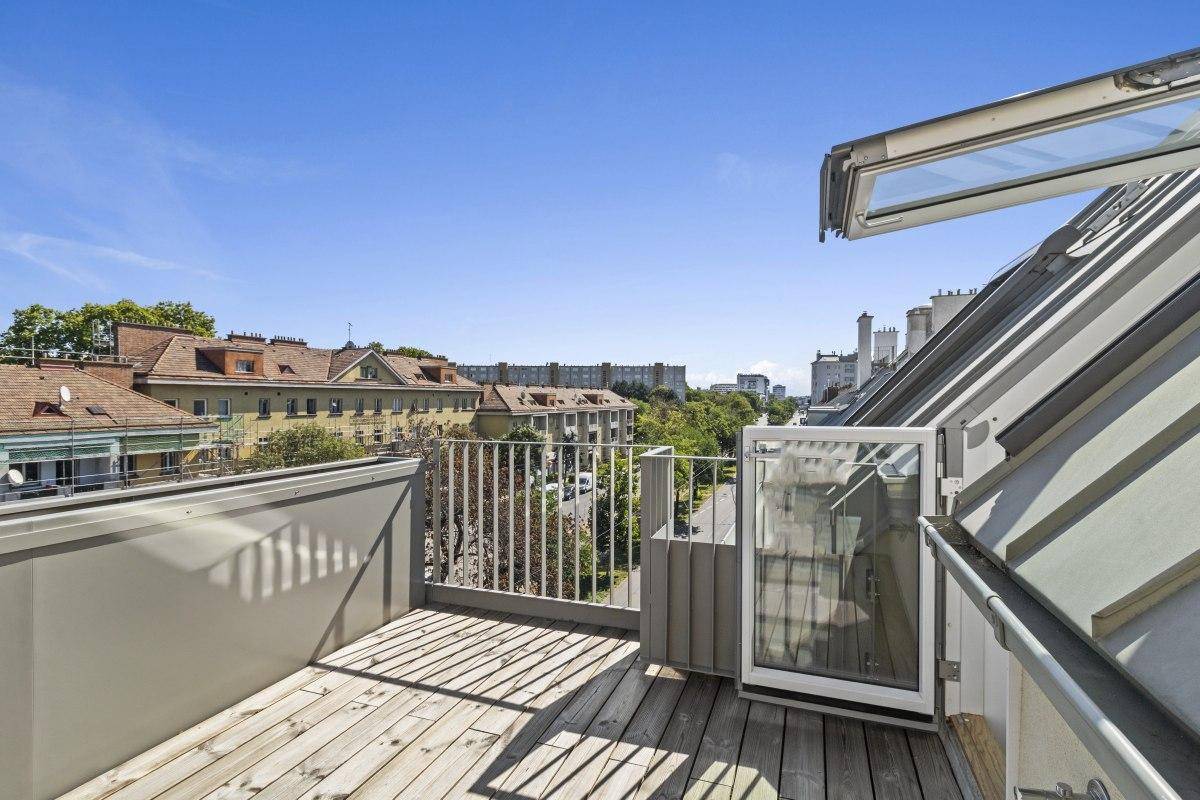 Balkon mit Holzboden und Blick über die Dächer der Stadt, zugänglich durch eine Tür.