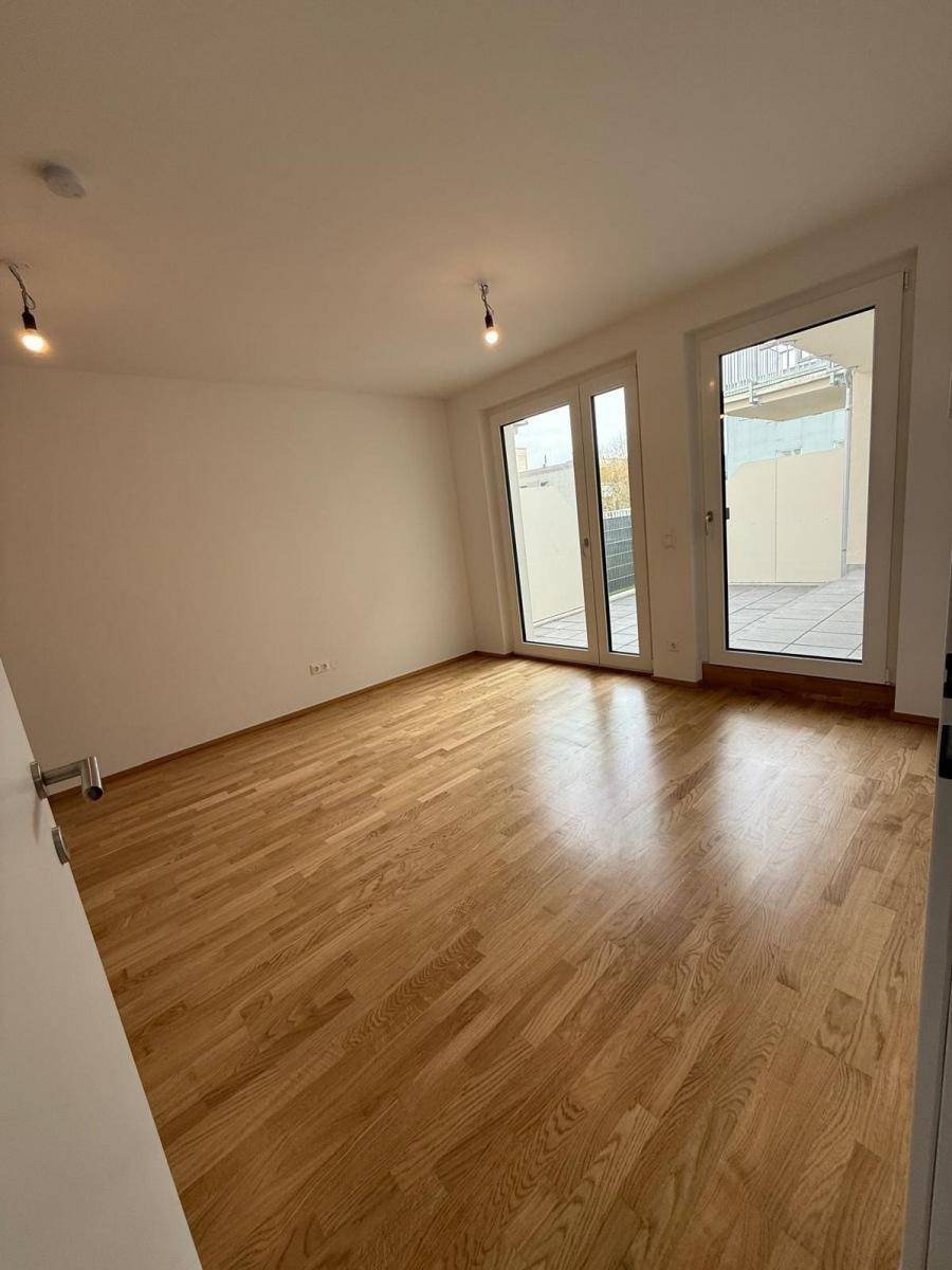 Heller Raum mit Eichenparkett und großen Fenstertüren, die zu einer Terrasse führen.