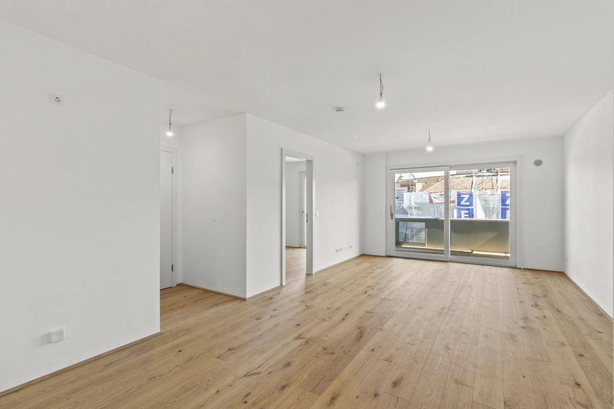 Heller, leerer Wohnraum mit modernem Holzboden und Zugang zu einem Balkon.