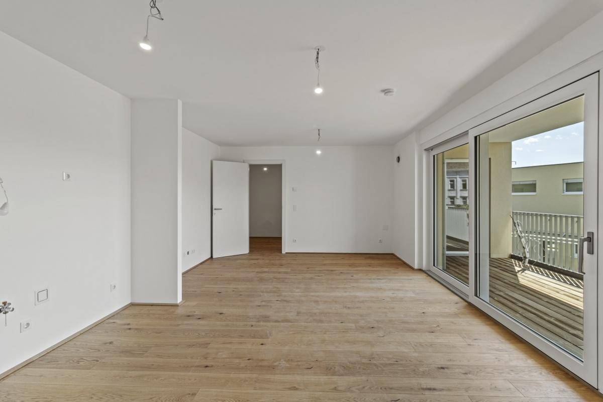 Geräumiger, unmöblierter Raum mit Holzboden und breiter Fensterfront zum Außenbereich.