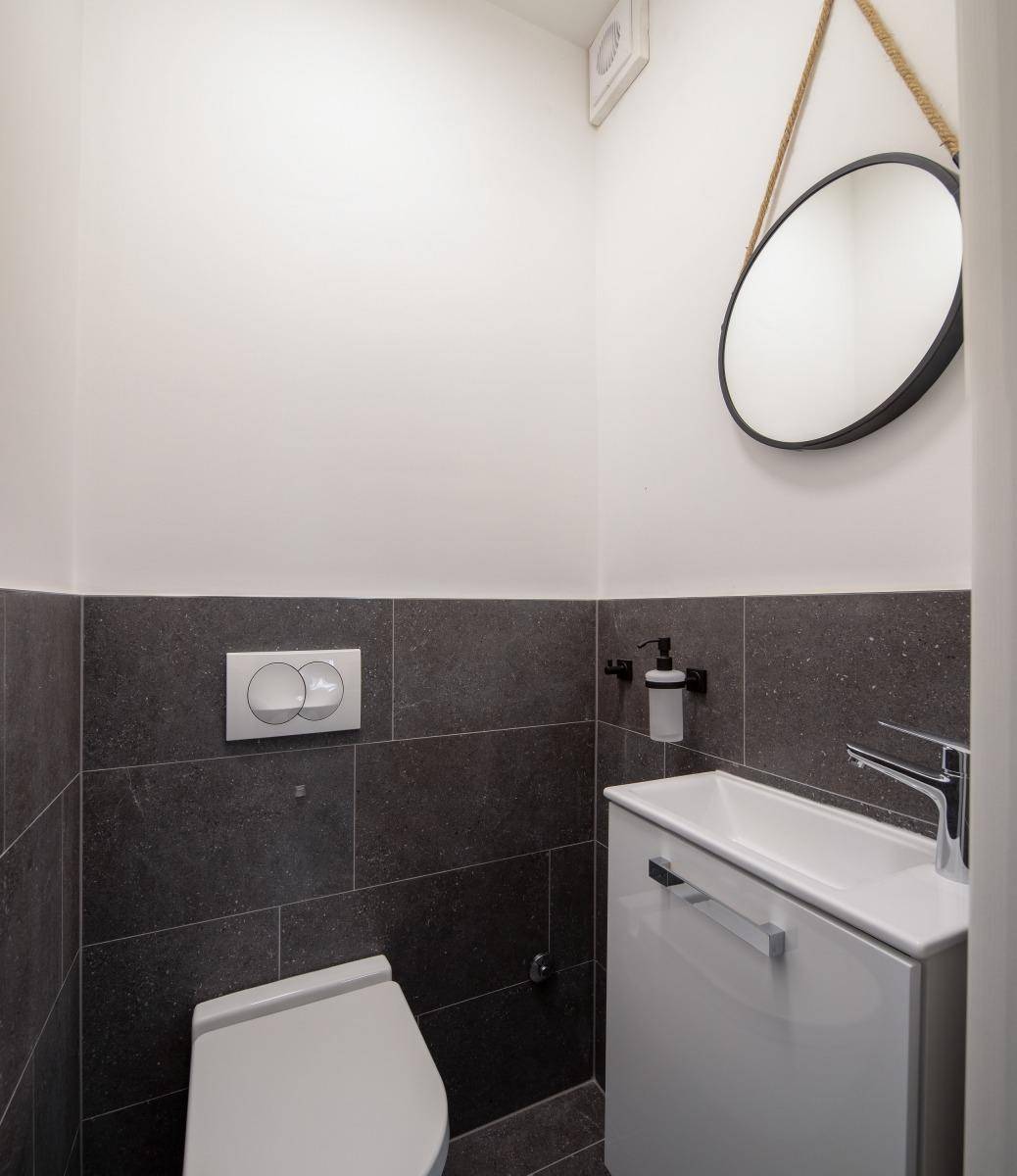 Kleines Gäste-WC mit Wand-WC, kleinem Waschbecken und modernem Spiegel.