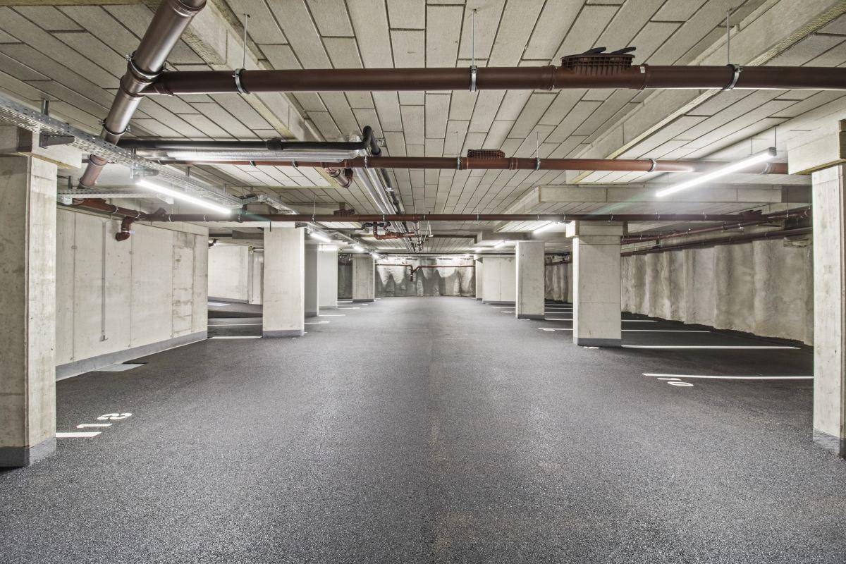 Geräumige Tiefgarage mit vielen Stellplätzen und sichtbaren Installationen an der Decke.