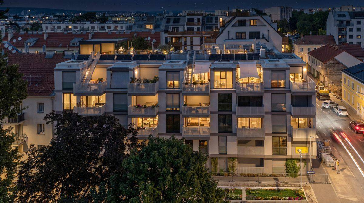 Moderne Wohnanlage bei Nacht mit beleuchteten Balkonen und Fenstern.